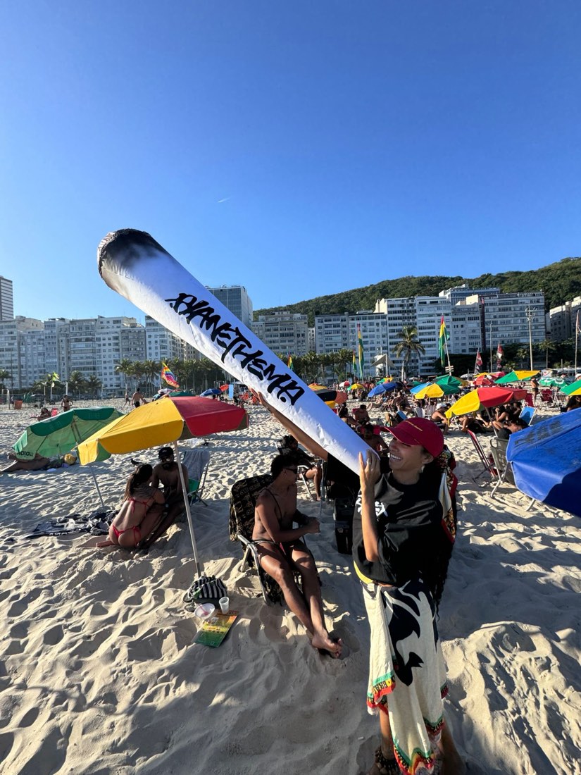 Tchele de boné vermelho erguendo um inflável gigante do Planet Hemp na areia lotada da Praia do Leme.