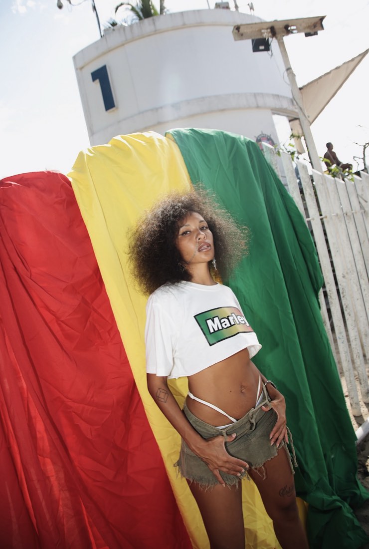 Tchele de camiseta Marley diante de um tecido vermelho, amarelo e verde, no Posto 1 do Leme, na campanha Redley × Bob Marley.